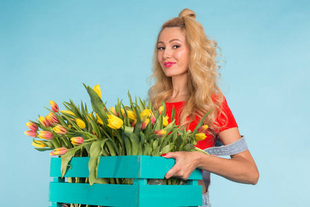 欢快的年轻金发女子花店与盒子的郁金香在蓝色背景