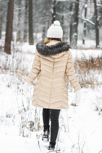 冬季衣服的年轻愉快的妇女在雪地森林散步