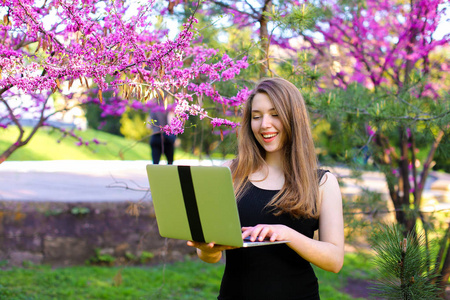 美丽的女性人使用笔记本电脑在绽放的背景