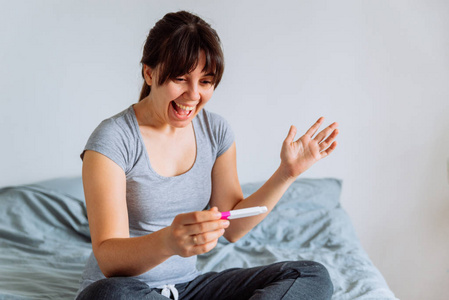 年轻快乐的妇女坐在床上看阳性妊娠试验