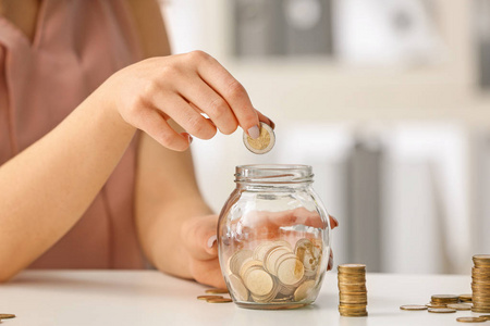 女人把硬币放在桌上的玻璃罐子里。储蓄概念