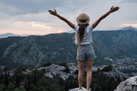 上升到天空。年轻的旅行妇女戴着帽子坐在高高的山顶上, 傍晚与日落。Montenegr