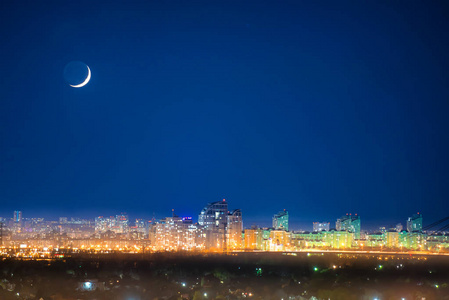 城市在晚上与新月在深蓝天空与星