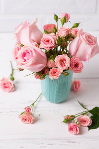 粉红色的玫瑰花在蓝色杯子对白色墙壁。花静物。选择性对焦。垂直图像