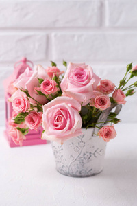 一束嫩粉色的玫瑰花, 装饰着粉红色的灯笼, 反对白砖墙。花静物。选择性对焦。文本的位置。垂直图像