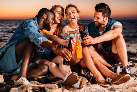 快乐的年轻人在日落时分一起在沙滩上消磨时光, 喝杯饮料。
