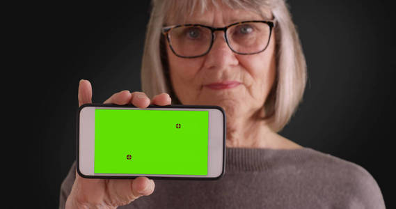 老年白人妇女拿着电话与绿色屏幕在灰色背景