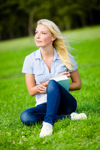 女孩拿着本书坐在草地上