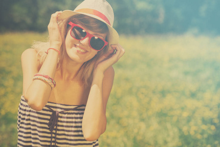 愉快的微笑的妇女在帽子和太阳镜在草甸享用