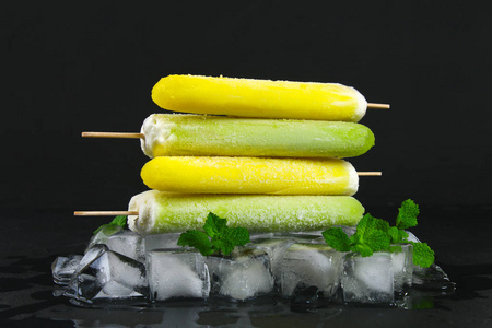 黄色和绿色水果冰淇淋在一根棍子与薄荷在冰在黑桌上