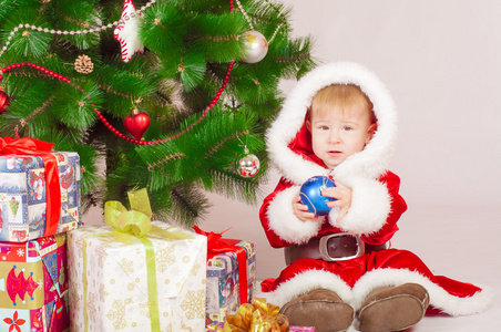 在与礼物的圣诞树圣诞老人服装的婴儿
