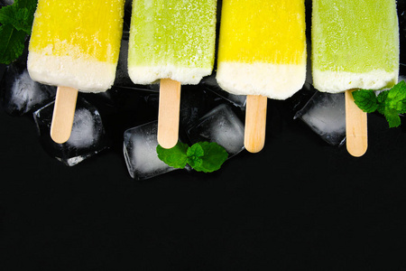 黄色和绿色水果冰淇淋在一根棍子与薄荷在冰在黑桌上