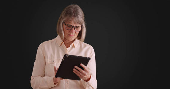 独立的高级妇女使用平板设备在灰色背景下在线浏览