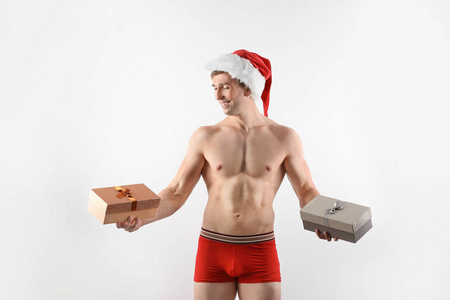 年轻肌肉男子在圣诞老人的帽子与礼品盒白色背景
