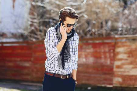 时尚的年轻男子在太阳镜与电话走在街上