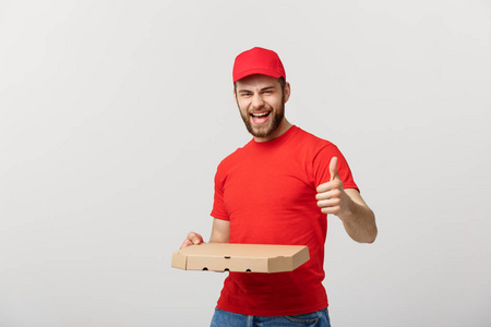 比萨送货的概念。年轻英俊的送货人显示比萨饼盒和持有拇指上的标志。在白色背景上被隔离