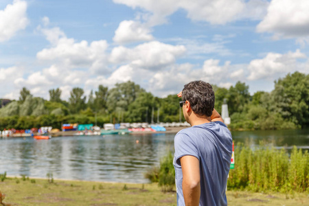 一个穿蓝色衬衣的男人在晴朗的日子里从一条河岸边看到一些东西。