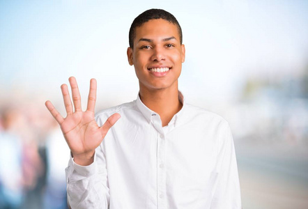 年轻的非洲裔美国人男子与白色衬衫计数五与手指在不聚焦的户外背景