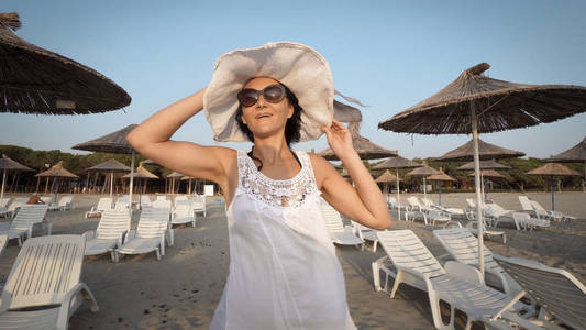 穿着白色连衣裙的女人在空沙滩上散步时戴着帽子