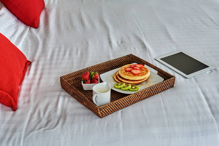 早餐托盘在未整理的床上与平板电脑在酒店房间。商务旅行理念