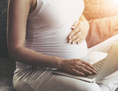 孕妇使用膝上型电脑和坐在沙发上