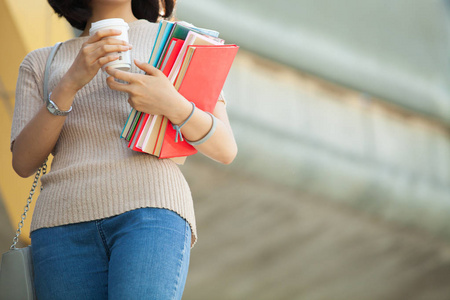 美丽的亚洲女大学生拿着她的书和一杯咖啡站在户外, 人们教育学习高中计划聪明的青少年概念