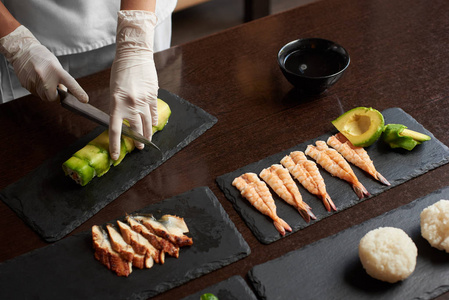 滚动寿司制作过程的特写视图。手在黑石板上切辊