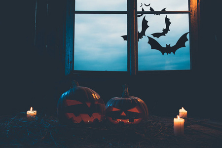 万圣节南瓜和蜡烛在一个废弃的木制房子的叶子和木板与温暖和冷的辉光, 对背景下的一个神秘的天空和蝙蝠的窗口