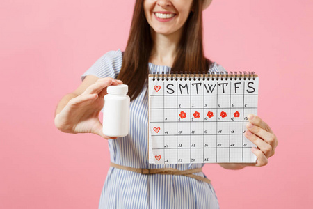 妇女在蓝色礼服被裁剪的相片举行白色瓶子用药片, 女性期间日历, 检查月经在背景被隔绝的天。医疗保健妇科概念。复制空间
