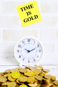 用时间写的黄色粘音符的选择性焦点是黄金与表时钟和金硬币在白色木质背景
