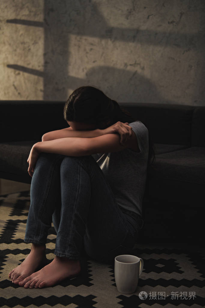 坐在沙发地板上的情感哭泣的妇女拥抱她的膝盖