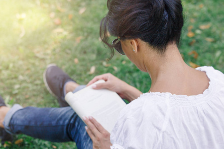 一个女孩在公园里看书。在绿色草地上的公园里平静的心情和放松的概念。穿着蓝色牛仔裤的中年妇女
