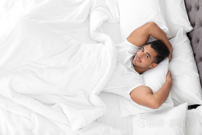 年轻人躺在床上柔软的枕头在家里, 顶部视图
