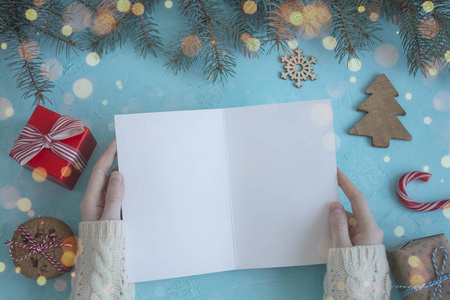 女性手穿着白色毛衣, 在蓝色背景上保留一张圣诞卡