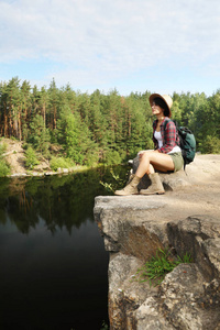 湖和森林附近岩石的年轻妇女。野营季节