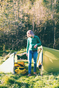 帐篷附近的女孩。在森林里露营。那个女人离开了帐篷。带着背包和帐篷旅行。早晨在自然的觉醒