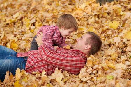 父子两人躺在黄叶上, 在秋城公园玩得很开心。他们摆姿势, 微笑着, 玩耍。明亮的黄色树