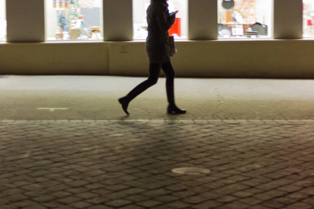 模糊的女士步行购物和看智能手机在商店前在11月的晚上