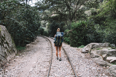 在山流浪徒步旅行期间, 女游客带着大背包去铁路。带背包的年轻女子旅行者探索自然野性的环境享受旅行