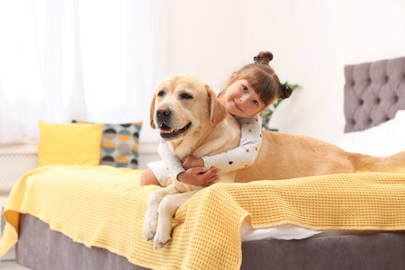 可爱的黄色拉布拉多猎犬和小女孩在床上在家