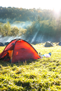 在露营地的橙色帐篷。在大自然中休息。在绿色草地上露营。黎明在森林里