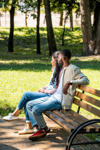 非洲裔美国人夫妇坐在木凳上的公园, 看着远离