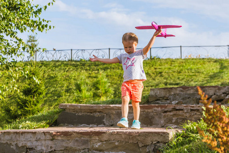 快乐的童年。Llittle 甜美的女孩沿着公园的石阶奔跑在一个阳光明媚的夏日, 带着一架粉红色飞机的玩具。