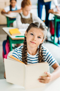美丽的小女孩与书看照相机在学校期间