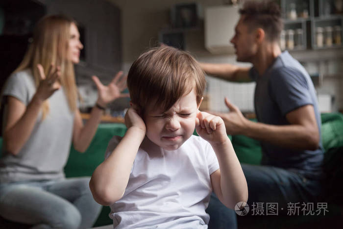 沮丧的孩子儿子在父母吵架时把手指放在耳朵上.