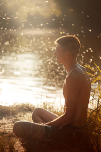 一个穿着黑色短裤躯干的年轻人坐在河岸上看书, medetiruet 日落