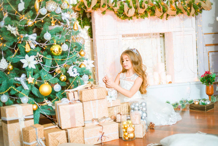 可爱的小女孩与长卷曲的头发在家里附近的圣诞树与礼品和花环和装饰的壁炉