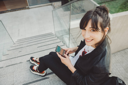 年轻漂亮的女人坐在楼梯上的城市和使用她的智能手机