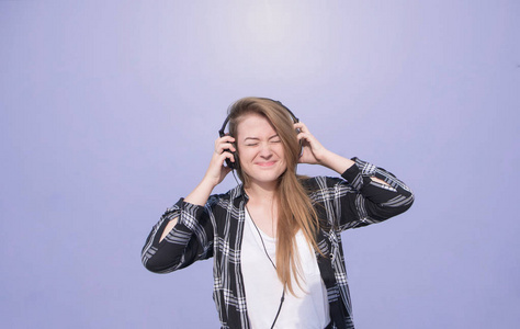 情绪快乐的女孩用耳机在他的头上站在紫色, 明亮的背景和听音乐。穿着便服的学生在紫色墙的背景上听音乐