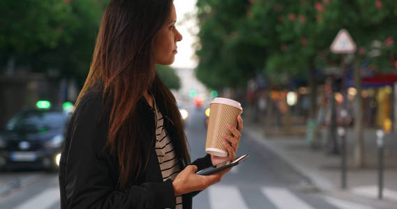 千禧年女性与她的咖啡用手机发短信, 而在城市街道